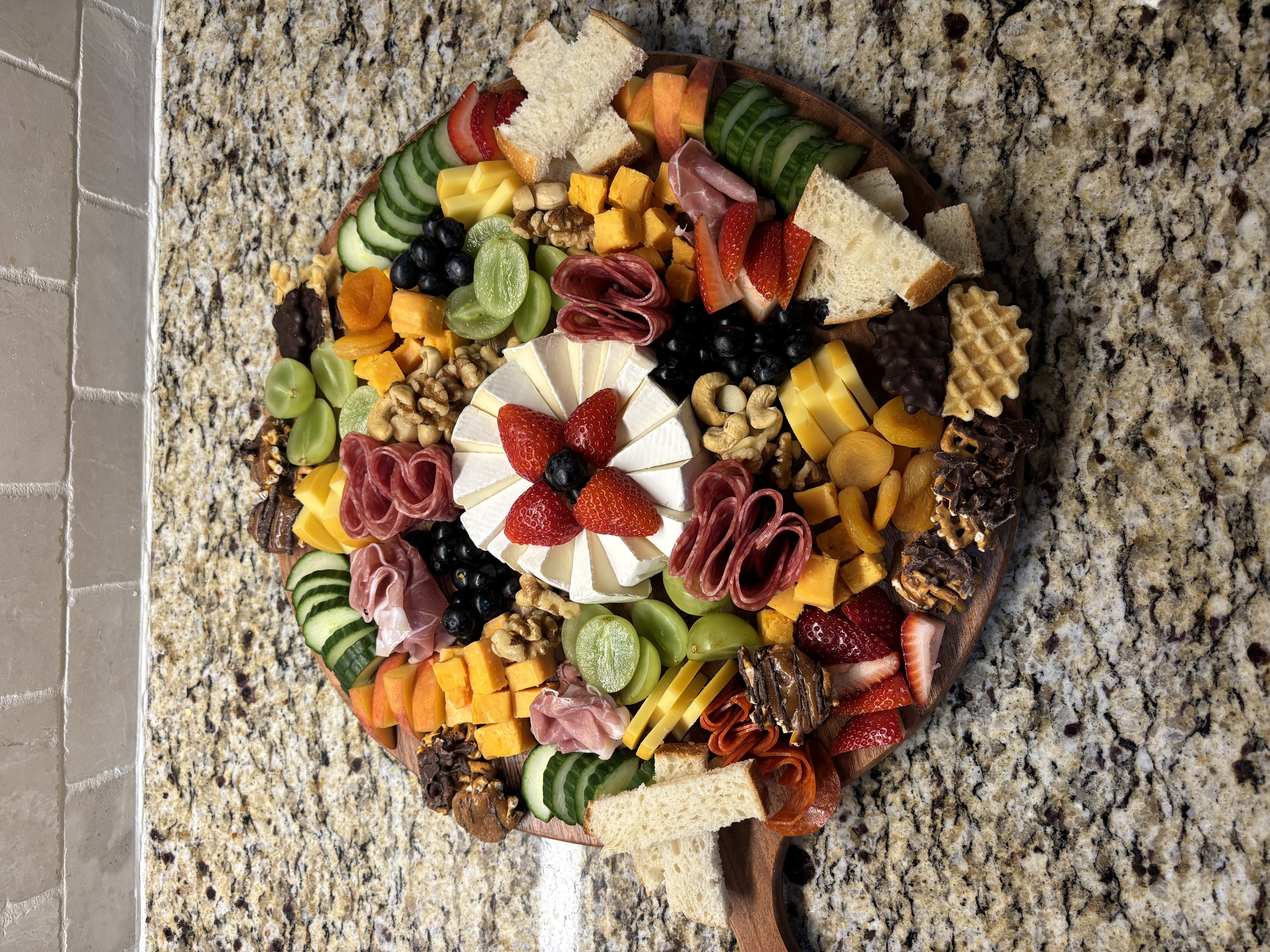 Round charcuterie board with brie, meats, fruit, vegetables, and nuts
