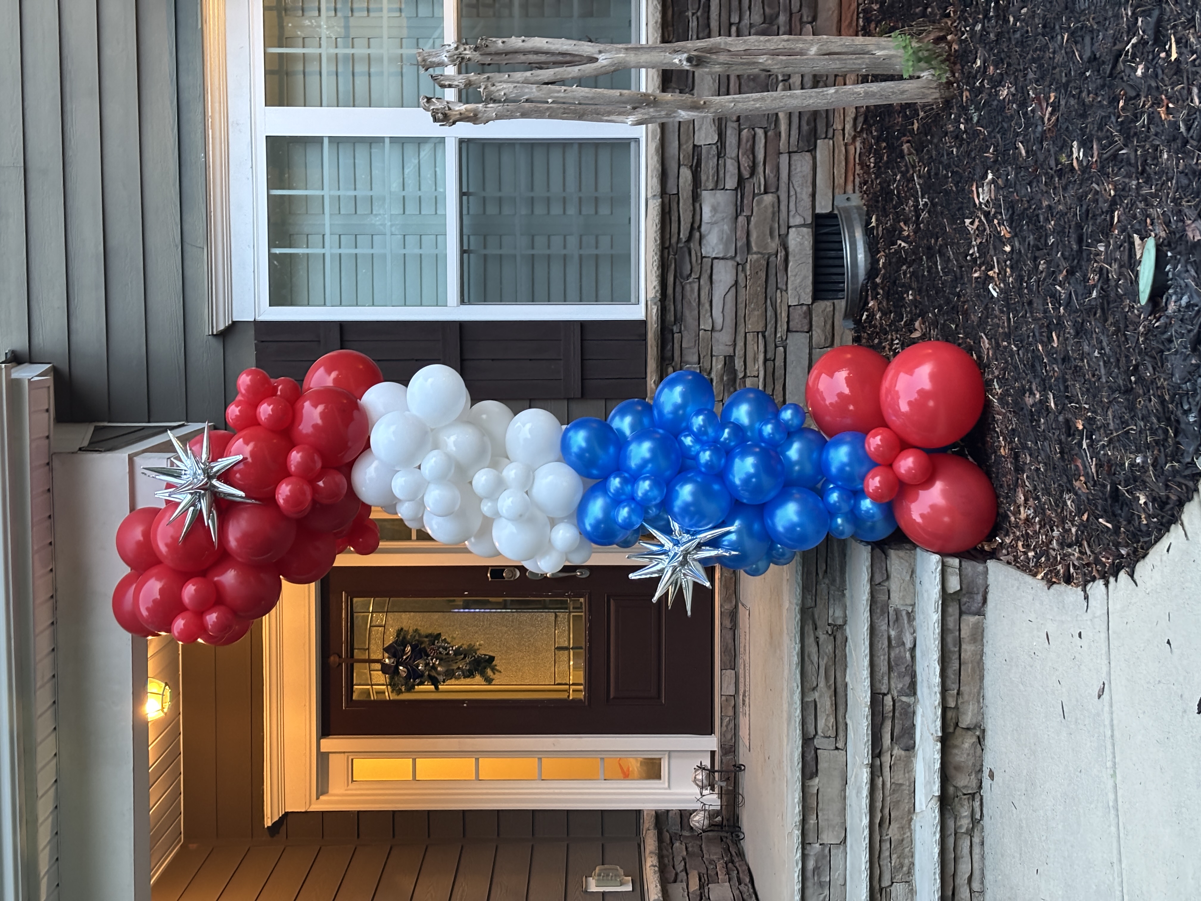 Red, white, and blue balloon column with silver star accents at a front entrance