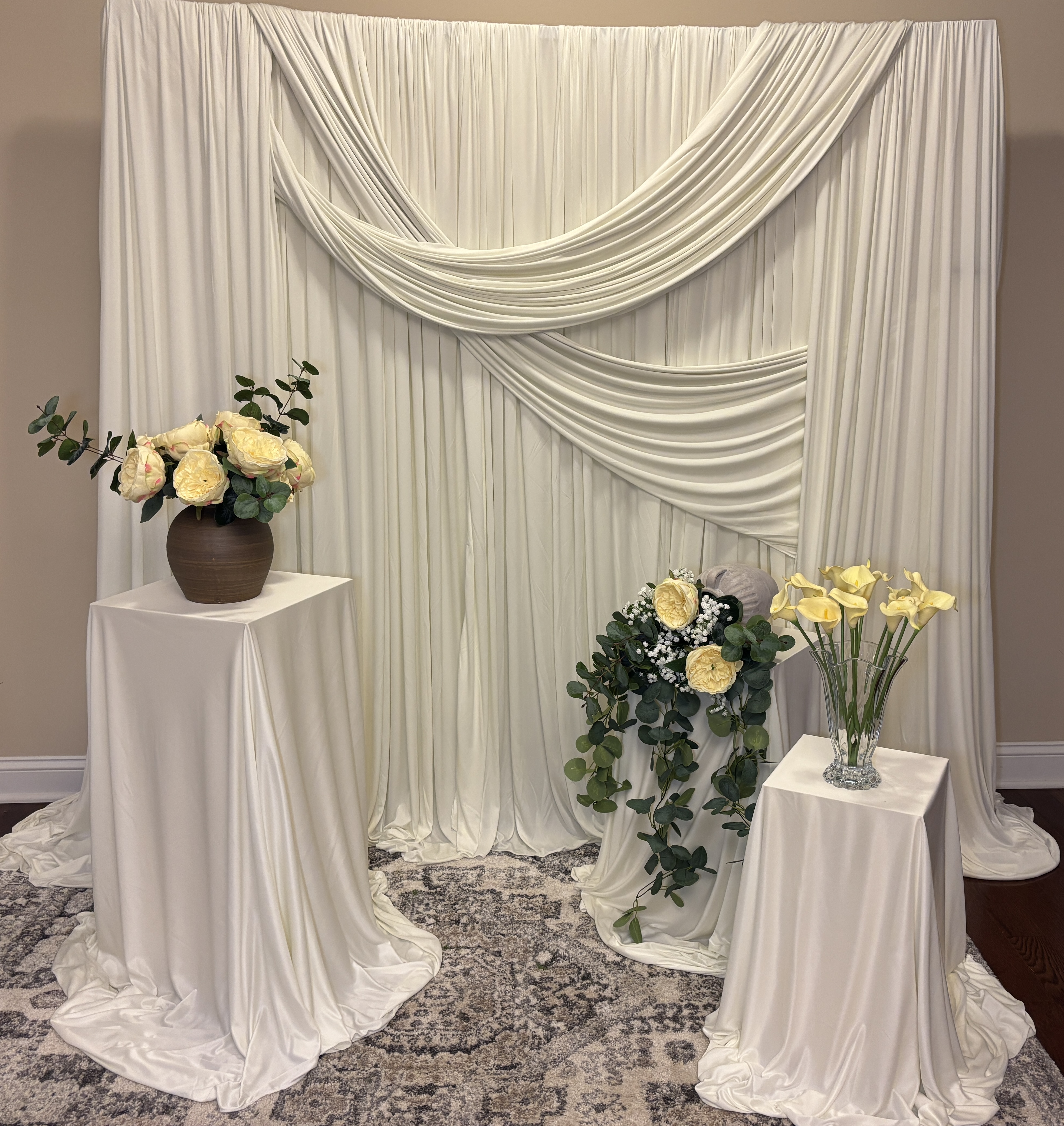 Ivory draped backdrop with yellow florals and greenery on three pedestals