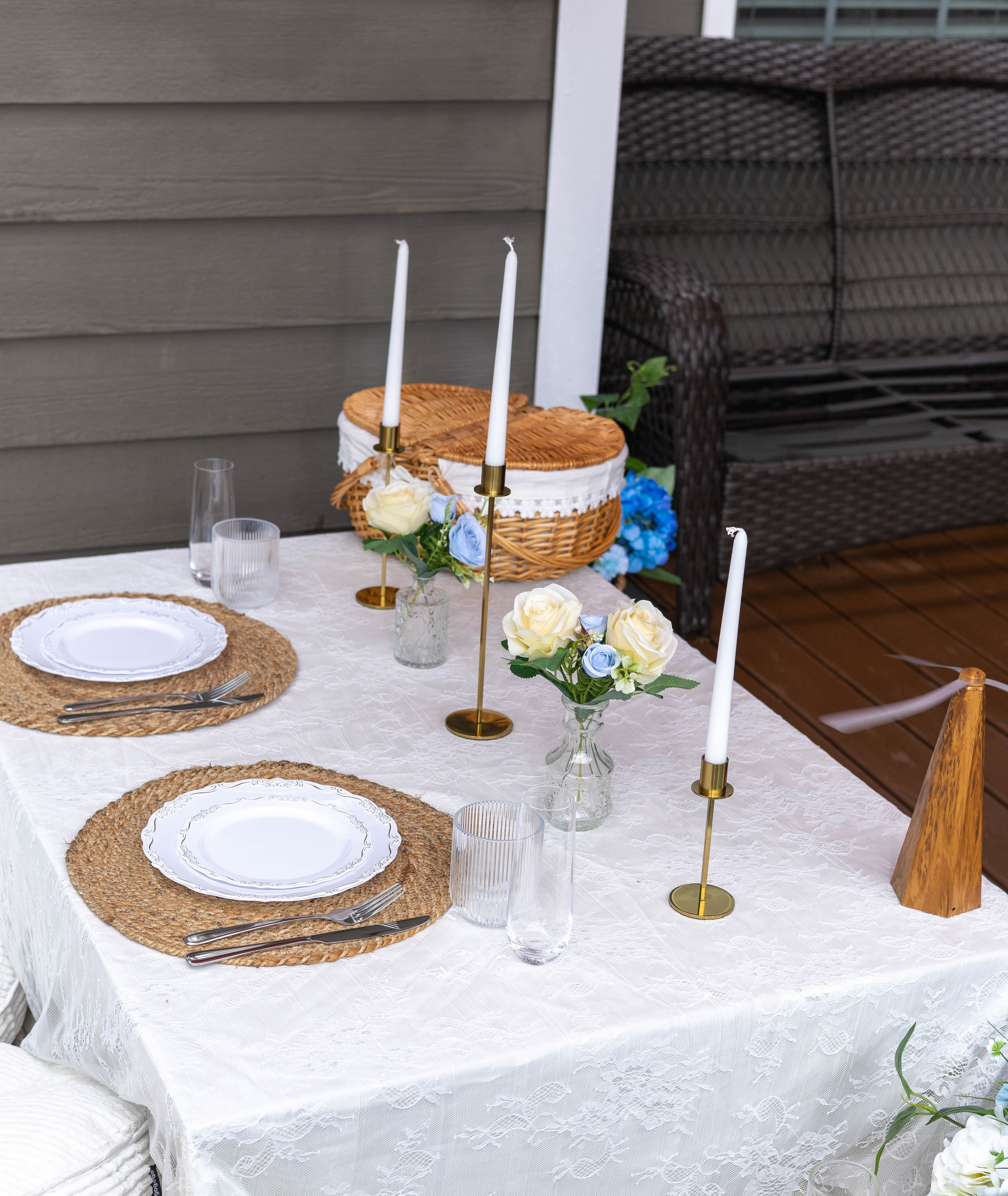 Lace-covered tablescape with woven chargers, blue and white roses, and gold candlesticks
