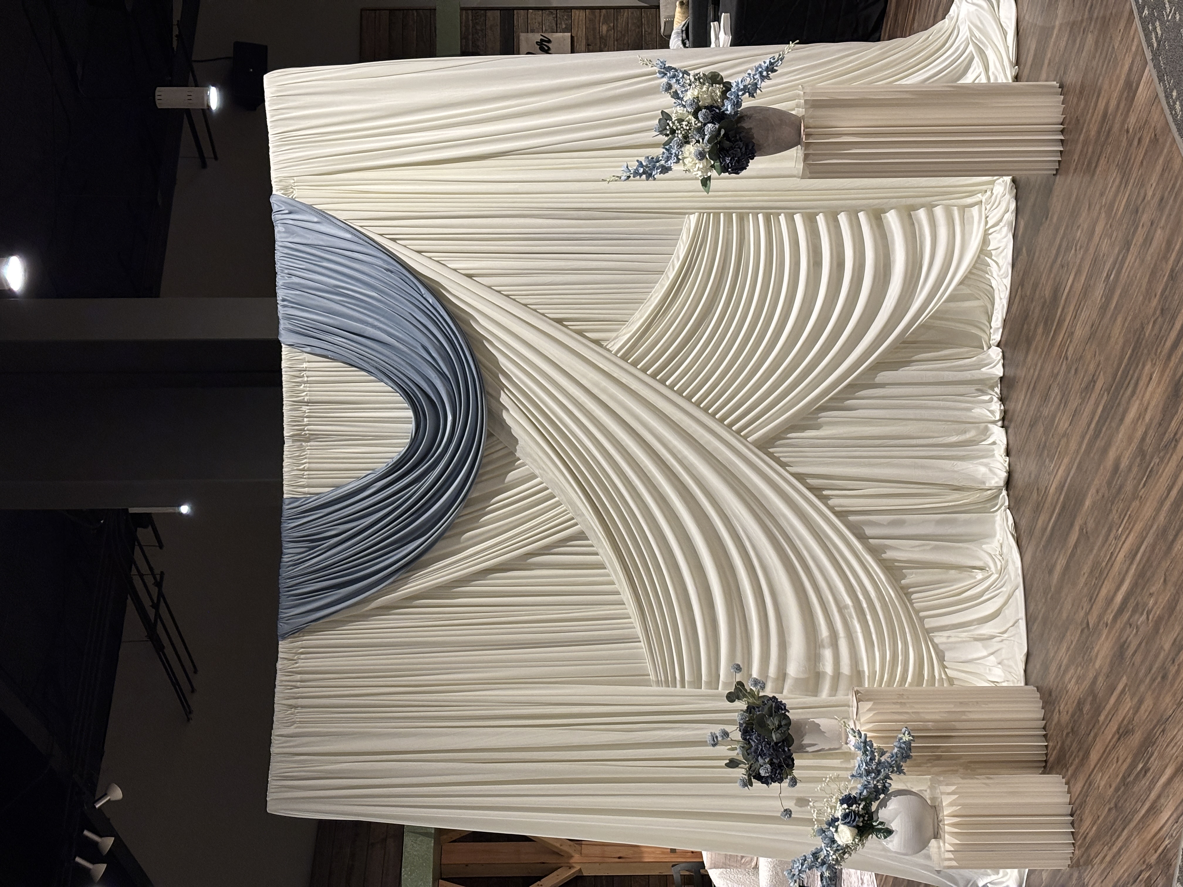 Ivory and dusty blue draped backdrop with blue and white floral arrangements
