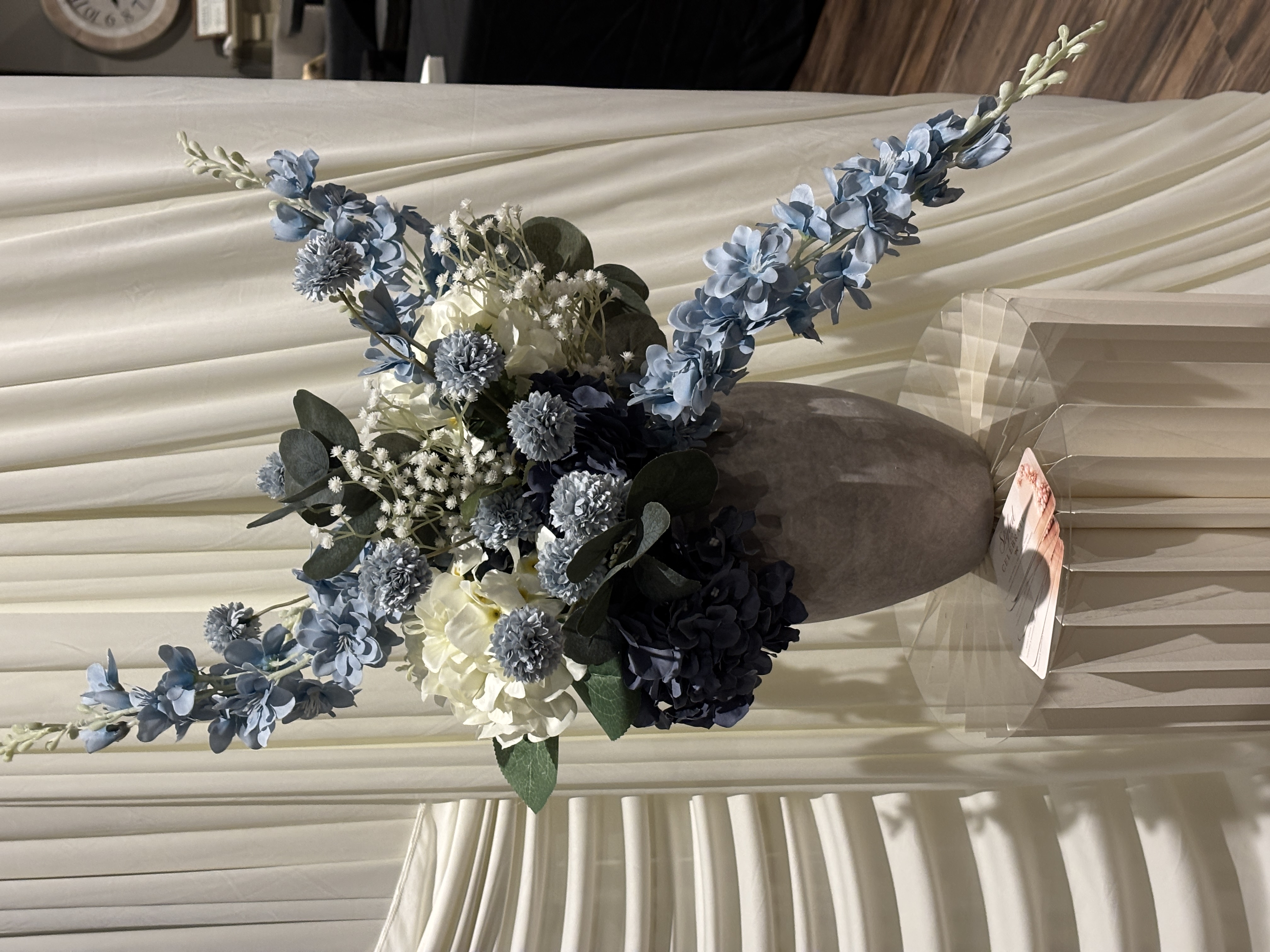 Blue and white floral arrangement on a pleated pedestal beside ivory draping