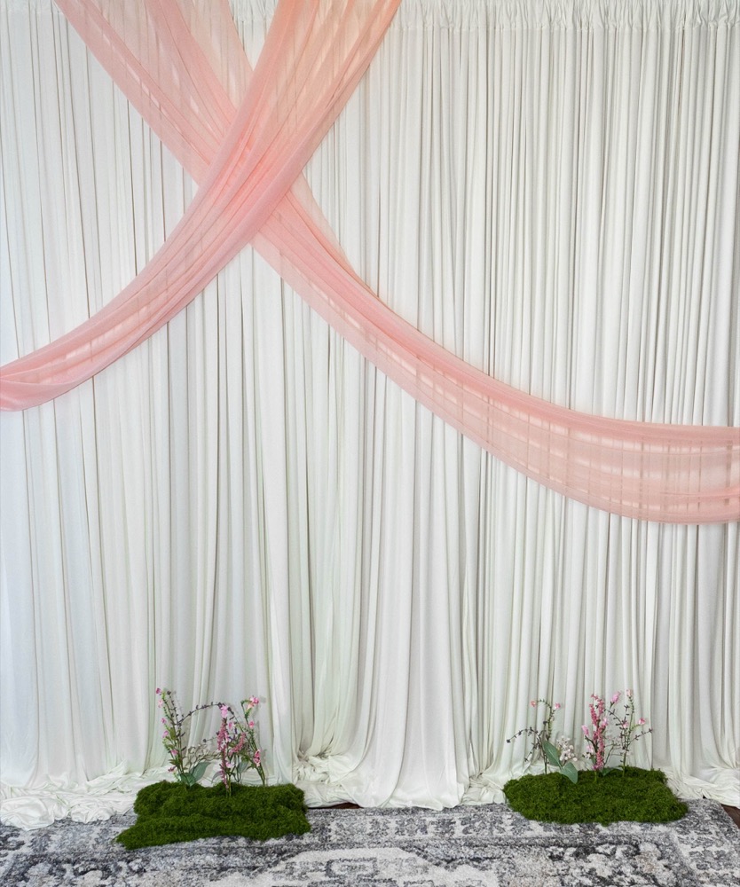 Draped curtain backdrop with crossed blush sash and moss floral accents